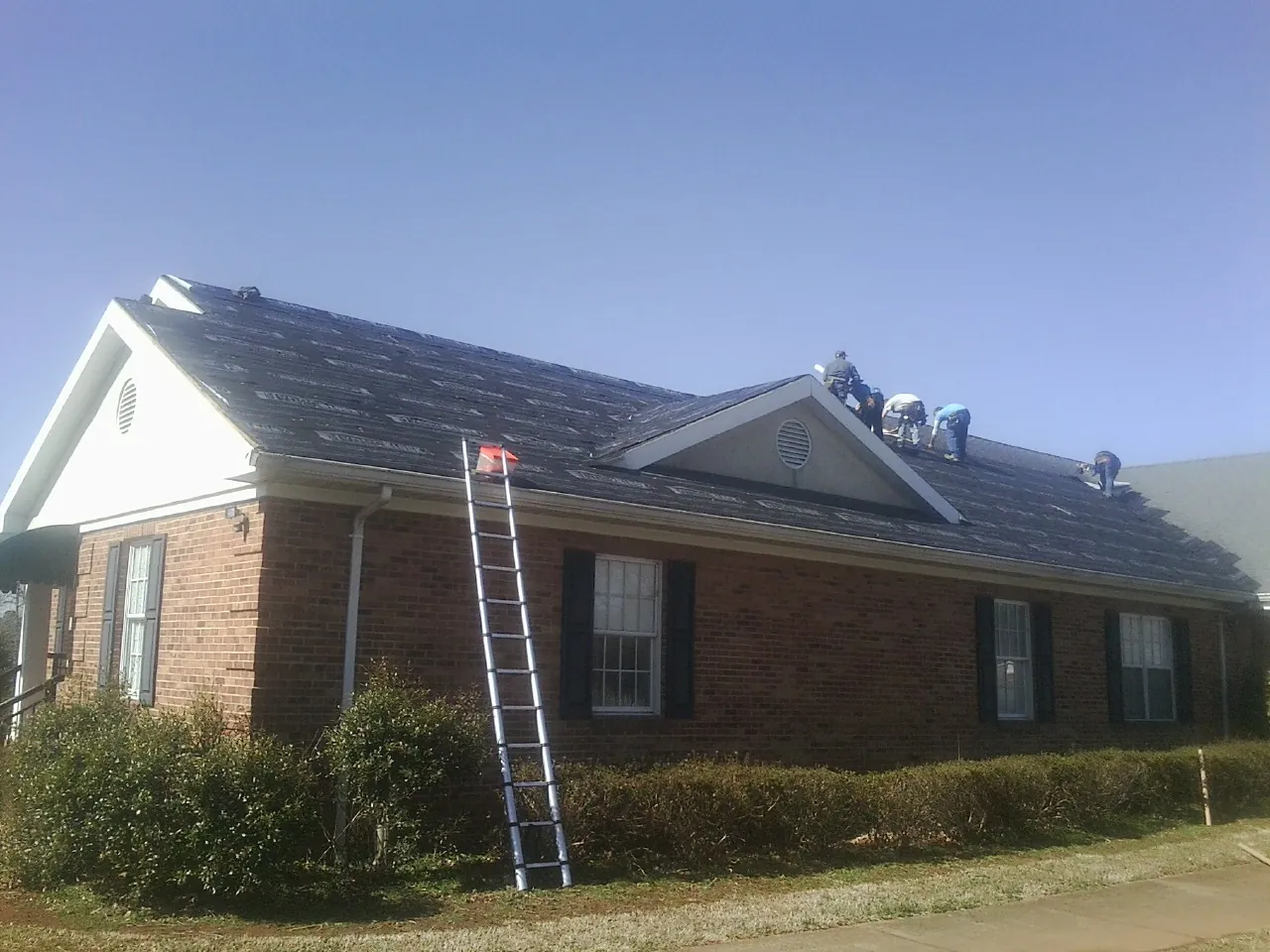 Crew tearing shingles off a brick ranch roof with a ladder set — Emergency Roof Repair work by our crew in Burtonsville