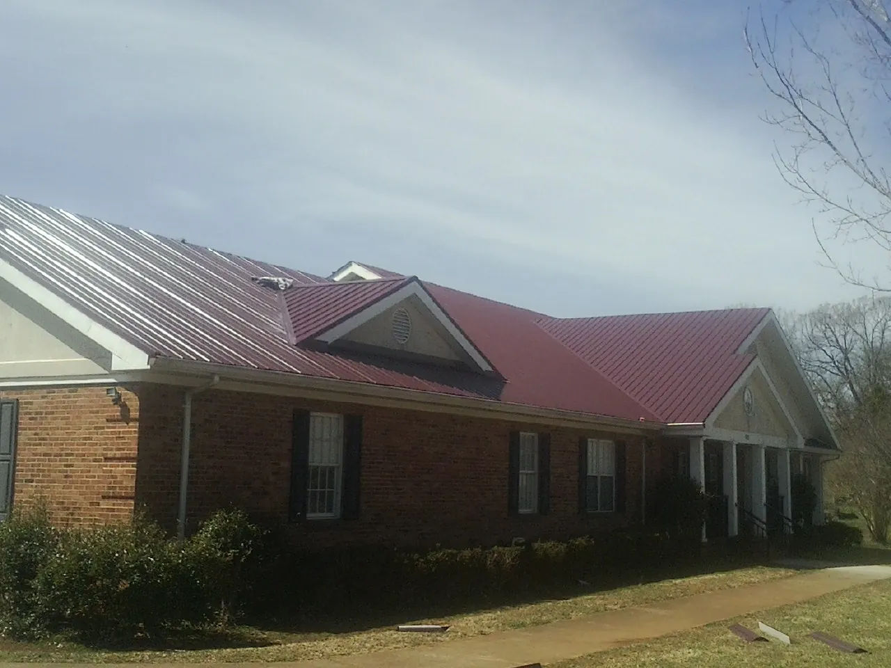 Red metal roof with gabled entries on a long brick building, from a Hail Damage Roof Repair job in Burtonsville