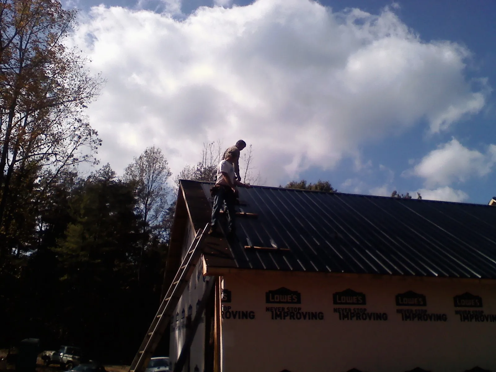 Roofer fastening dark metal panels high against a cloudy sky, from a Roof Inspection job in Burtonsville