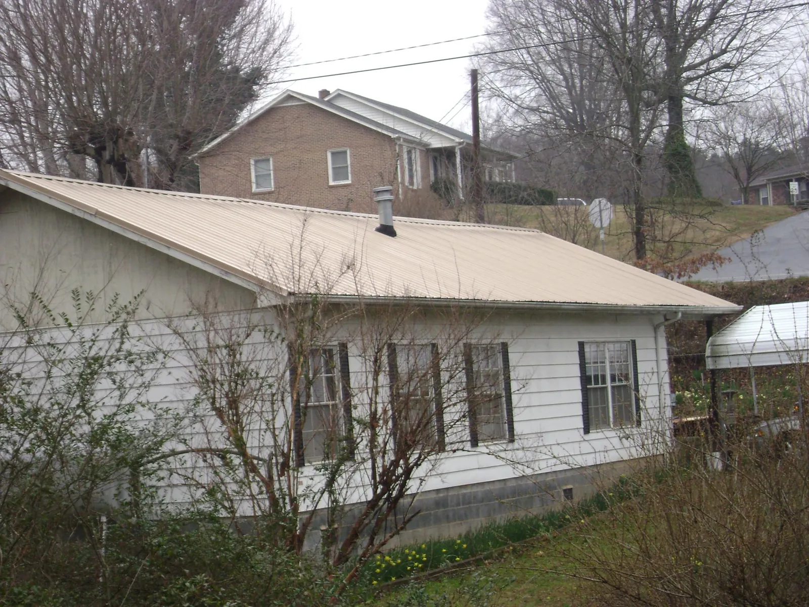 Tan metal roof on a white sided house set into a hillside — Commercial Roofing by Roofing Brothers in Burtonsville
